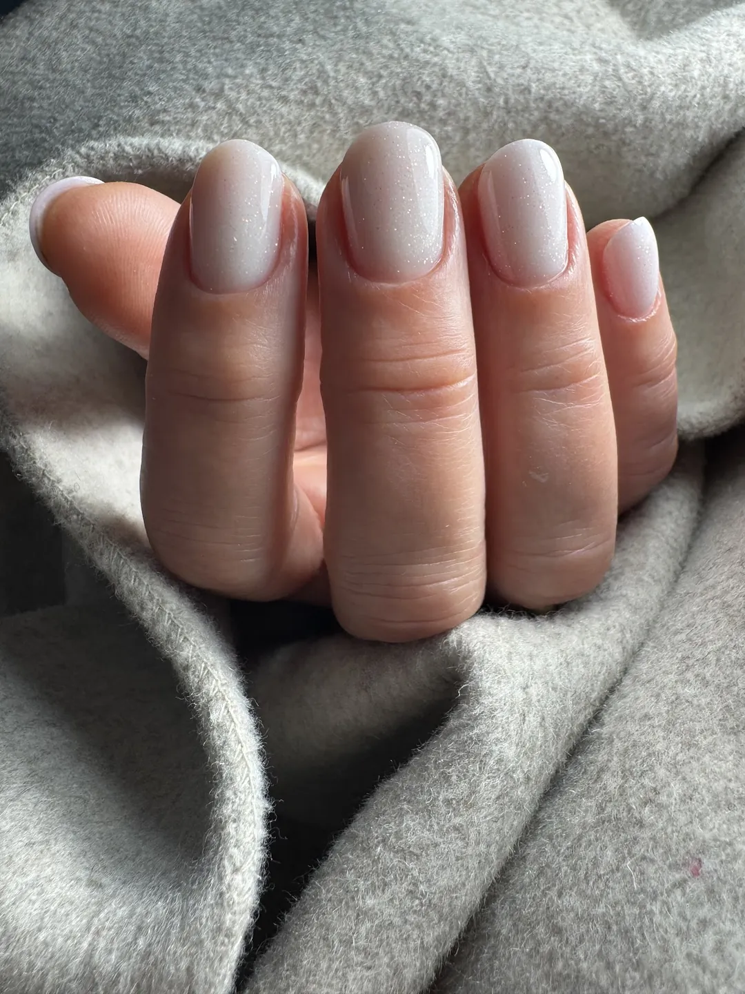 Une pose nude laiteuse, ongles courts arrondis, sur un pull gris