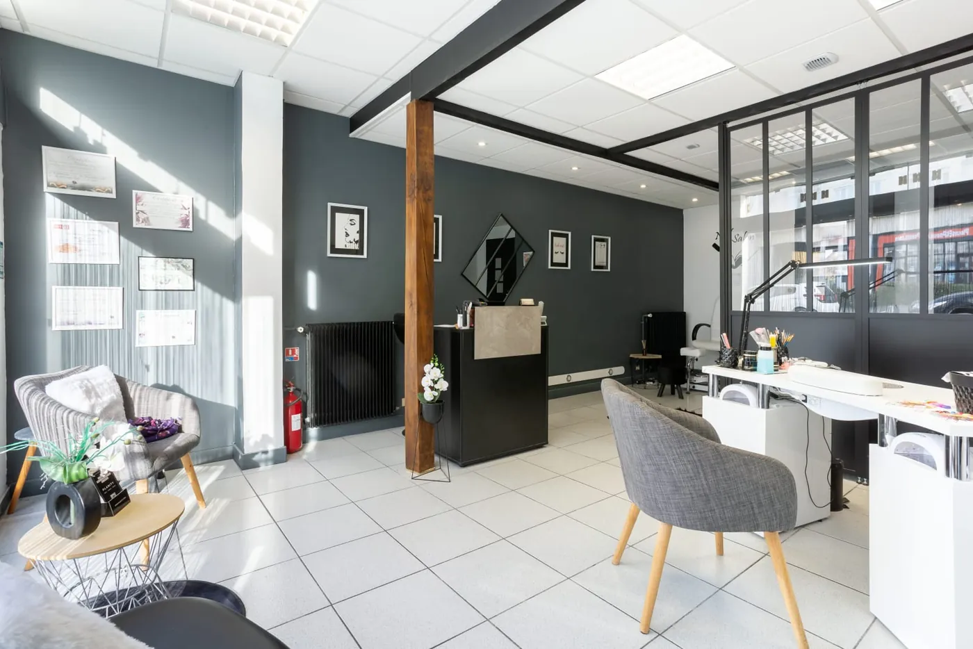 L'intérieur du salon : poste ongles, fauteuils gris, murs ardoise et verrière noire